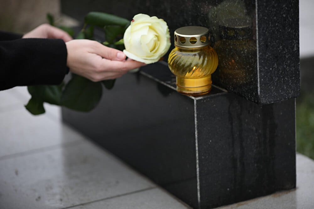Woman holding white rose near black granite tombstone with candle outdoors, closeup. Funeral ceremony.　出典：123rf